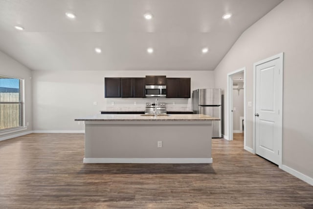 kitchen featuring appliances with stainless steel finishes, dark brown cabinets, a center island with sink, and lofted ceiling