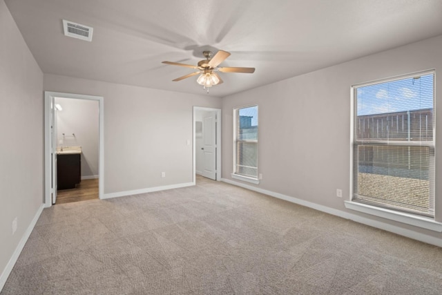 unfurnished bedroom featuring multiple windows, connected bathroom, light colored carpet, and ceiling fan