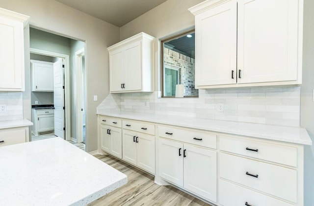 kitchen with light stone countertops, light wood-type flooring, decorative backsplash, and white cabinets