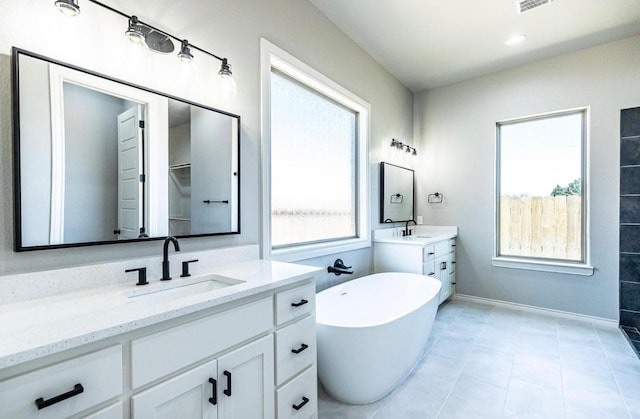 bathroom with a tub to relax in, tile patterned floors, vanity, and a wealth of natural light