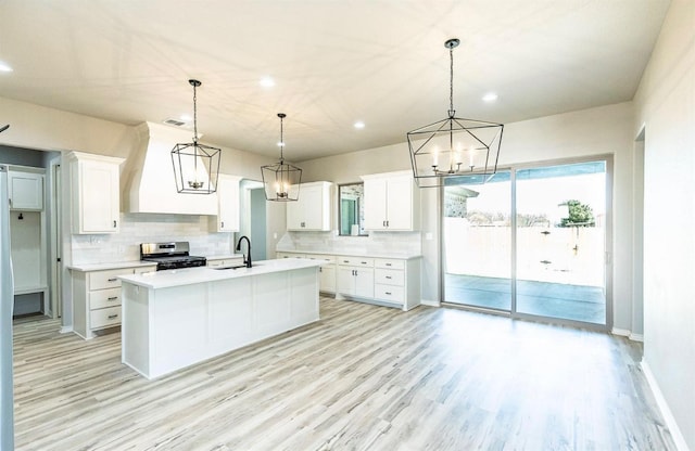 kitchen featuring hanging light fixtures, stainless steel range, an island with sink, and white cabinets