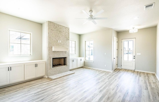 unfurnished living room featuring ceiling fan, a brick fireplace, and light wood-type flooring