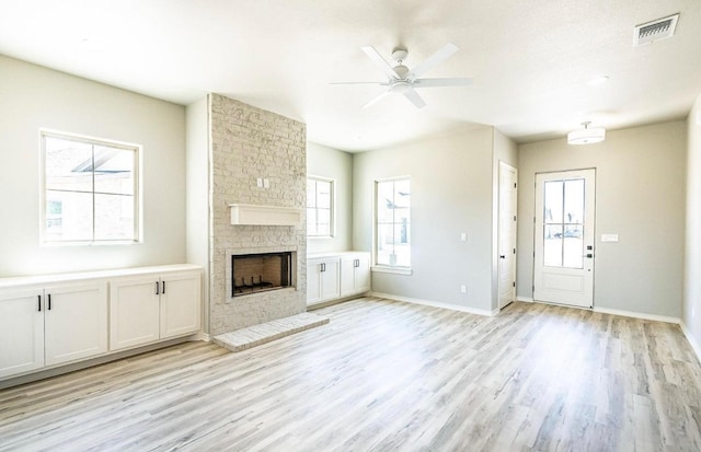 unfurnished living room with ceiling fan, a brick fireplace, and light hardwood / wood-style floors