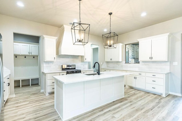 kitchen with sink, stainless steel stove, an island with sink, and white cabinets