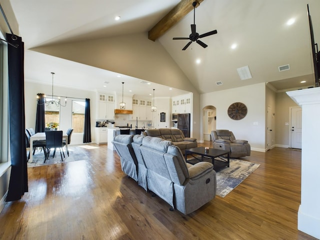 living room with dark wood-type flooring, beam ceiling, high vaulted ceiling, ornamental molding, and ceiling fan with notable chandelier