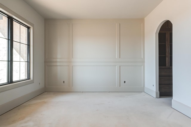 spare room featuring a decorative wall, unfinished concrete flooring, baseboards, and arched walkways