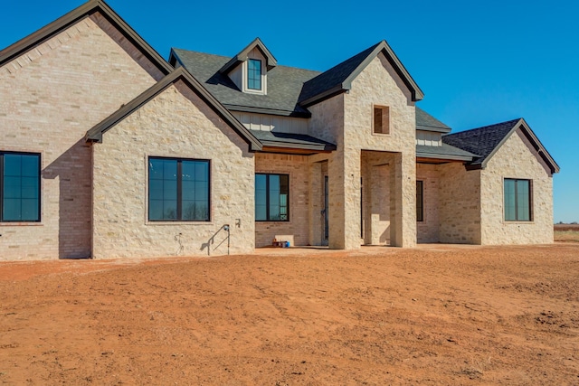 rear view of property featuring brick siding, stone siding, and a shingled roof