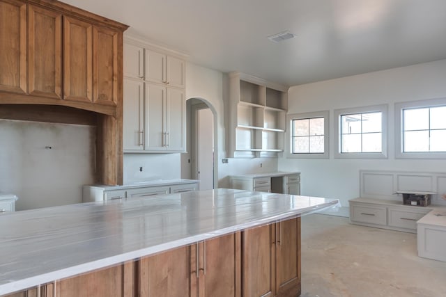 kitchen featuring visible vents, concrete floors, open shelves, arched walkways, and brown cabinets