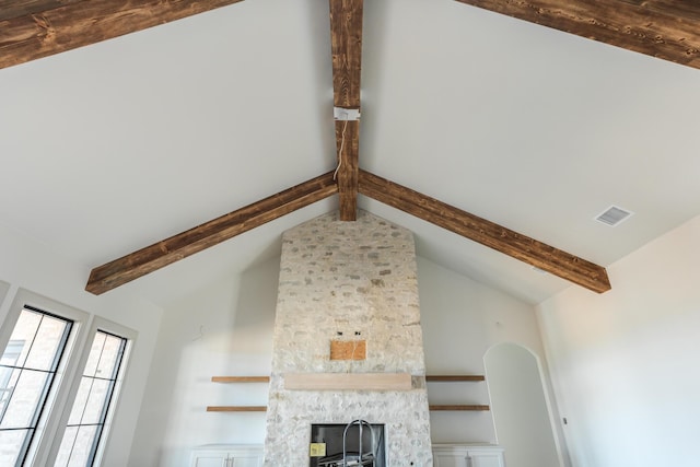 interior details featuring a stone fireplace, visible vents, and beamed ceiling