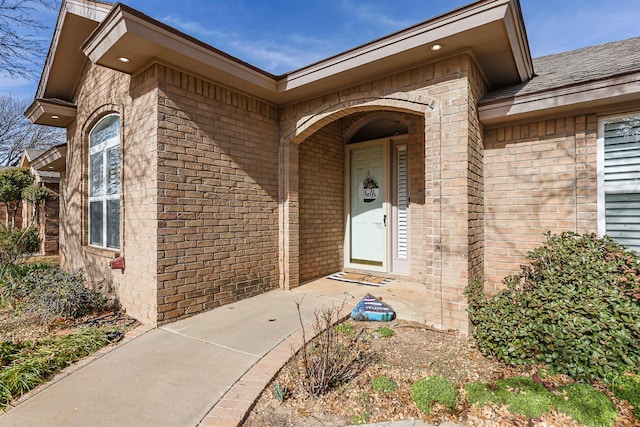 doorway to property featuring a shingled roof and brick siding