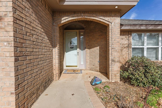 view of exterior entry with a shingled roof and brick siding