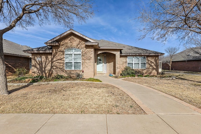 single story home featuring a shingled roof, a front yard, and brick siding