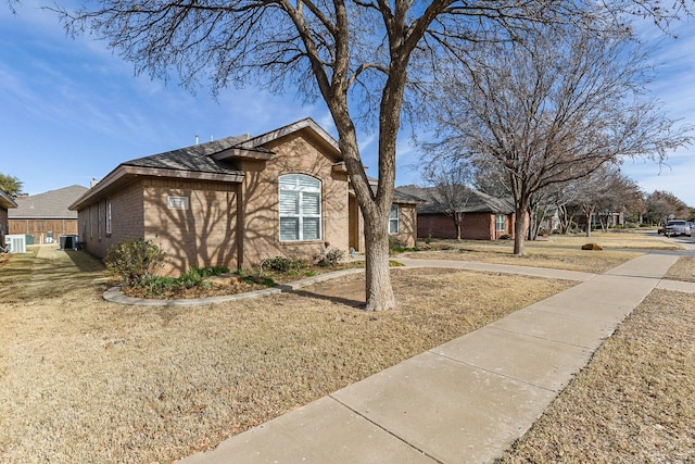 view of front of home with brick siding, a front lawn, and central AC unit