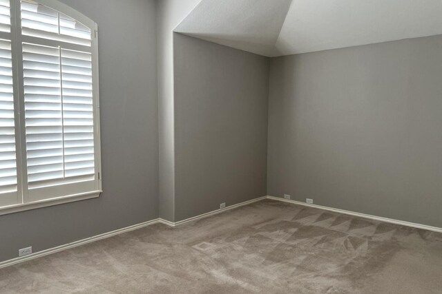 unfurnished room featuring light carpet, vaulted ceiling, and baseboards