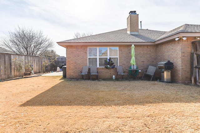 rear view of property with a chimney, roof with shingles, fence, a yard, and brick siding