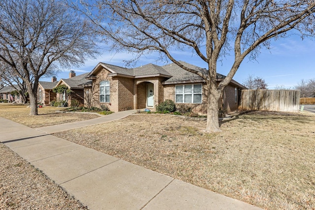 single story home featuring brick siding, roof with shingles, a front yard, and fence