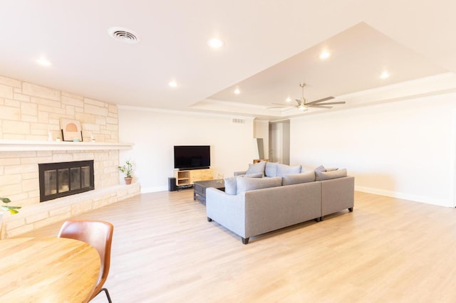 living room with crown molding, a tray ceiling, ceiling fan, a fireplace, and light hardwood / wood-style floors