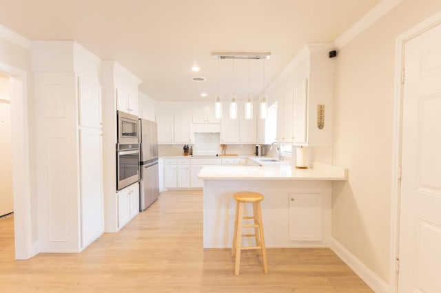 kitchen featuring appliances with stainless steel finishes, pendant lighting, white cabinetry, sink, and a kitchen breakfast bar