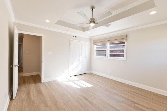 unfurnished bedroom with crown molding, a tray ceiling, and light wood-type flooring