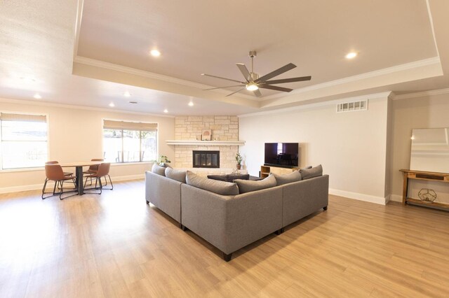 living room featuring crown molding, light hardwood / wood-style floors, a fireplace, and a tray ceiling