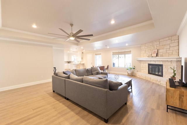 living room with a raised ceiling, crown molding, light wood-type flooring, and a fireplace