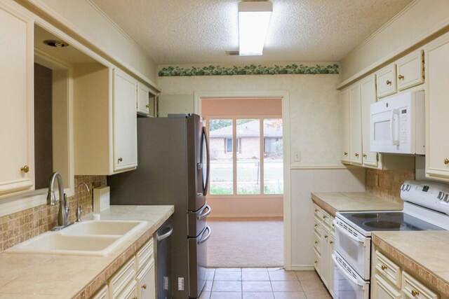 kitchen featuring sink, a textured ceiling, light tile patterned floors, white appliances, and white cabinets