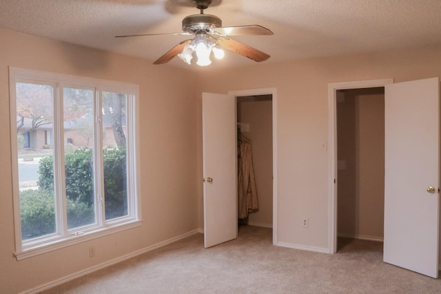 unfurnished bedroom featuring multiple windows, ceiling fan, light colored carpet, and a textured ceiling