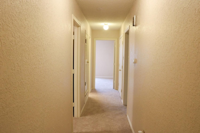 hallway with light carpet and a textured ceiling