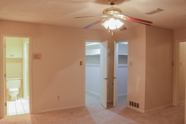 unfurnished bedroom featuring connected bathroom, a spacious closet, light colored carpet, and a textured ceiling