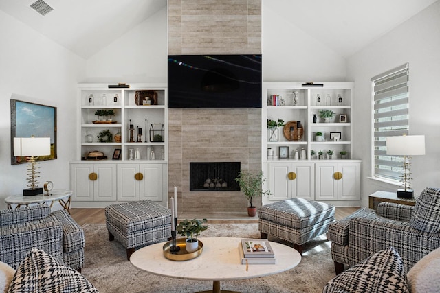 living room featuring a tiled fireplace, vaulted ceiling, and wood-type flooring