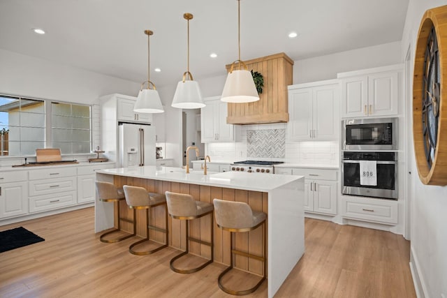 kitchen featuring white cabinetry, stainless steel oven, decorative light fixtures, a kitchen island with sink, and high end white fridge