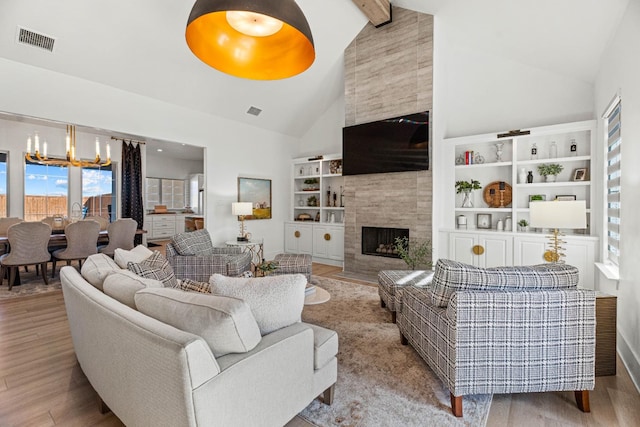 living room featuring high vaulted ceiling, beamed ceiling, a tiled fireplace, a notable chandelier, and light wood-type flooring