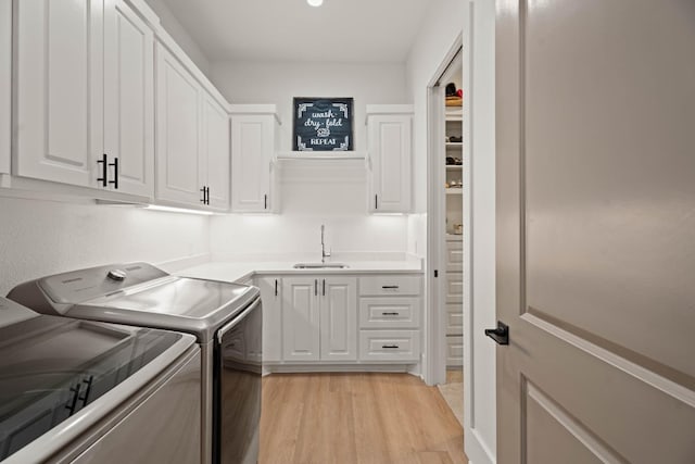 laundry room featuring cabinets, separate washer and dryer, sink, and light hardwood / wood-style floors