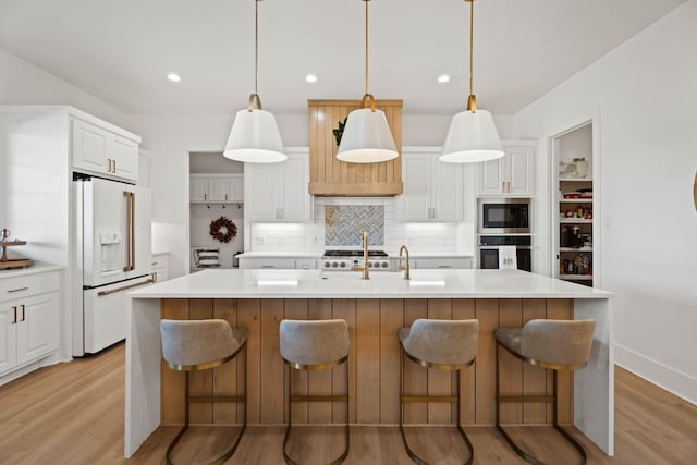 kitchen featuring high end fridge, white cabinetry, stainless steel oven, and a center island with sink