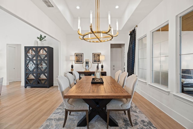 dining room with light wood-type flooring, a chandelier, and a tray ceiling