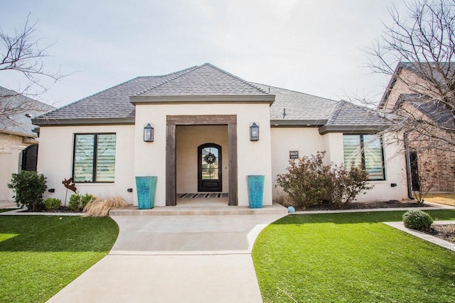 french country home with a shingled roof, a front lawn, and stucco siding