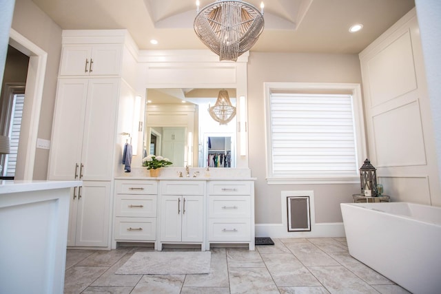 full bath with double vanity, recessed lighting, an inviting chandelier, a sink, and a freestanding tub