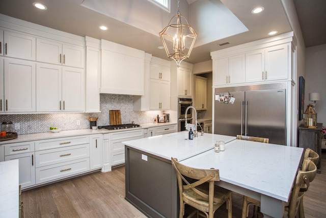 kitchen with white cabinets, an island with sink, appliances with stainless steel finishes, a breakfast bar area, and pendant lighting