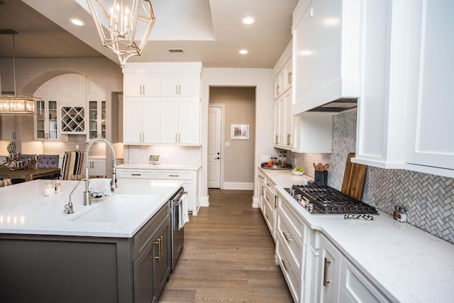 kitchen featuring a center island with sink, hanging light fixtures, glass insert cabinets, white cabinetry, and a sink