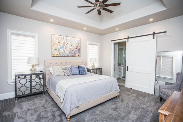 bedroom with dark colored carpet, a raised ceiling, recessed lighting, and a barn door