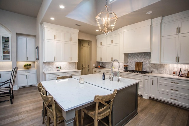 kitchen featuring an island with sink, dark wood-style floors, hanging light fixtures, white cabinetry, and stainless steel gas cooktop