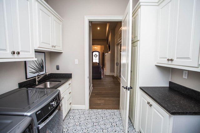 kitchen with washing machine and clothes dryer, dark countertops, a sink, and white cabinetry