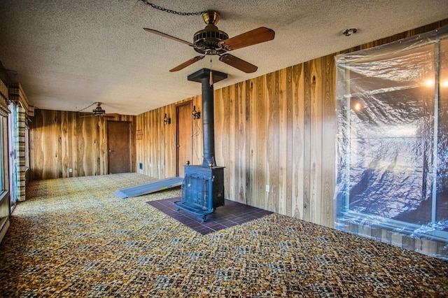 unfurnished living room featuring a wood stove, a textured ceiling, and wood walls