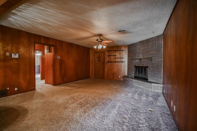 unfurnished living room featuring ceiling fan, wooden walls, a fireplace, a textured ceiling, and light carpet