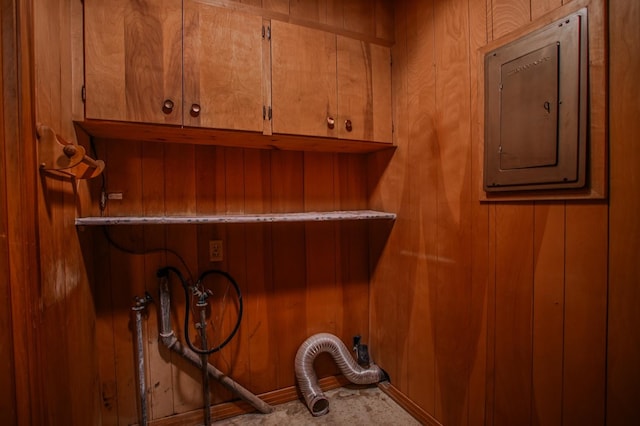 washroom featuring wooden walls, cabinets, electric panel, hookup for a washing machine, and electric dryer hookup