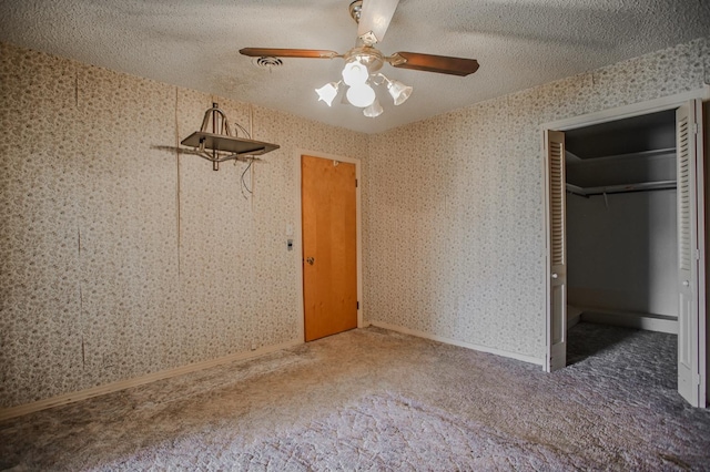 unfurnished bedroom with ceiling fan, dark colored carpet, a textured ceiling, a spacious closet, and a closet