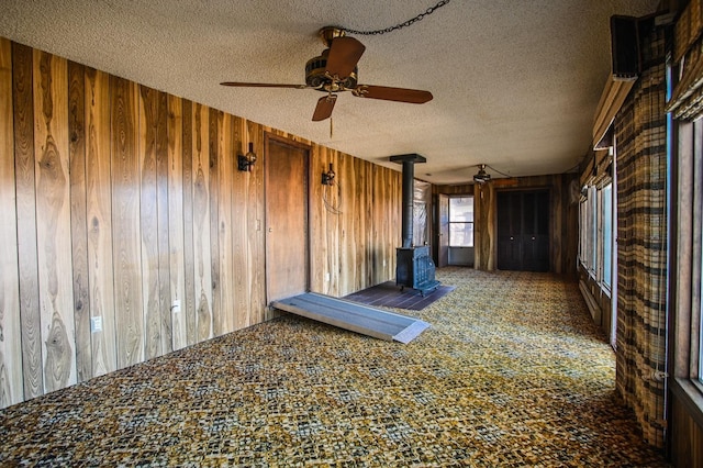 carpeted empty room featuring a textured ceiling, a wood stove, and wood walls