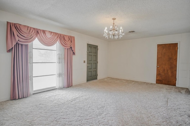 carpeted spare room featuring an inviting chandelier and a textured ceiling