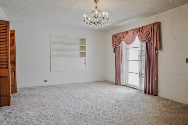 unfurnished room with carpet flooring, a notable chandelier, a textured ceiling, and built in shelves