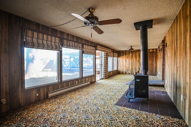 unfurnished sunroom featuring a baseboard heating unit, a wood stove, and ceiling fan